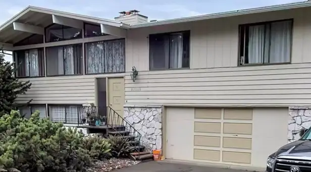 Two-story beige split-level house with a white garage door and stone accents before updates.